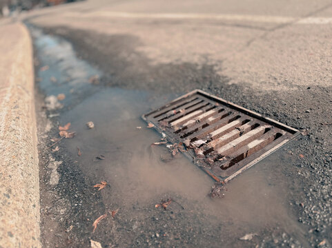 Une plaque d'&eacute;gout au milieu de la route, d'o&ugrave; s'&eacute;coule de l'eau. Mise au point s&eacute;lective.