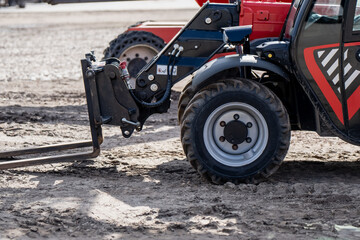 Red telehandler forklift with hydraulic arm and heavy duty tires parked on a muddy construction site for industrial material handling and urban infrastructure development © K