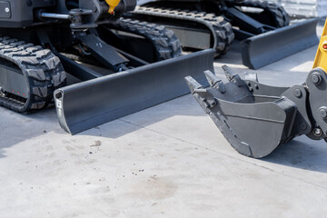 Tracked earthmoving machine with straight dozer blade and toothed digging bucket parked on concrete, excavation equipment for grading, trench work and site service © K