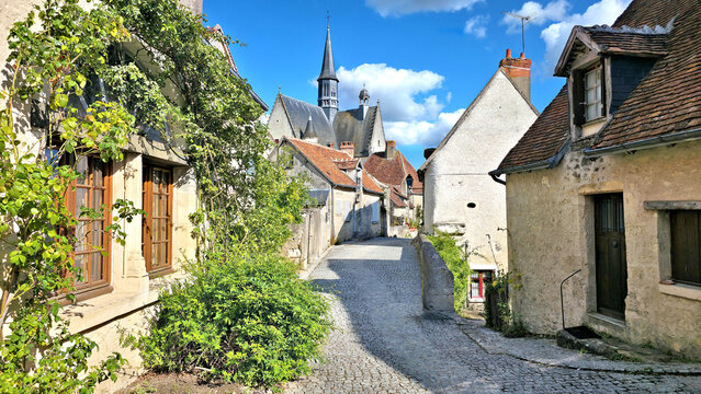 Beautiful streets of Montresor in the Loire Valley of France. Picturesque stone houses, leafy vines and church in the background.