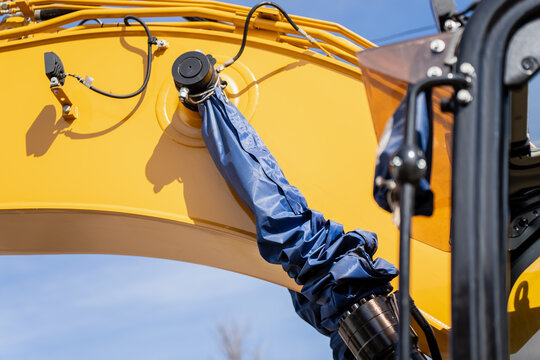 Curved yellow excavator arm section with blue cylinder cover, routed cables and fittings, heavy equipment detail for serviceability and reliable jobsite output