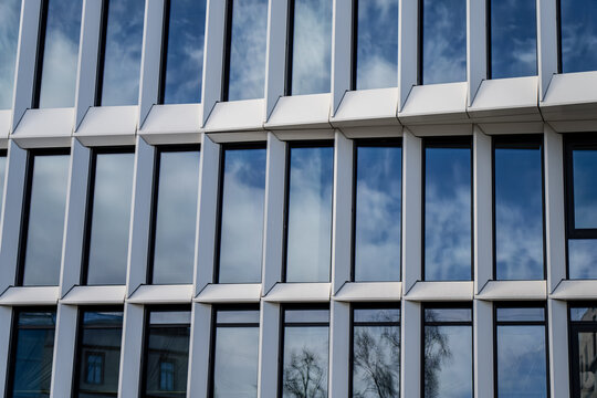 Modern white facade with repeating vertical window frames and blue reflective glass, contemporary office architecture and structured urban business design