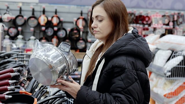 Customer shopping for a new saucepan in the cookware department of a supermarket, examining stainless steel kitchenware in a housewares store