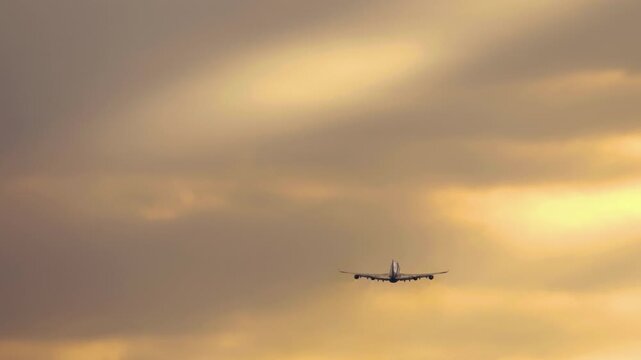 A large four-engine widebody jet aircraft is seen climbing through the sky during a stunning sunset or sunrise. Concepts ir travel and long-haul aviation.