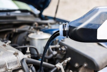 Fototapeta premium A person is pouring engine oil into a car. It’s happening at a garage or repair shop.