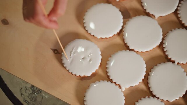 Hand testing iced mini pies for texture and glaze consistency with toothpick, inspection across batch of tartlets on countertop tray, glossy white icing, studio lighting, production vibe