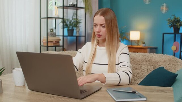 Caucasian woman at home on table working on laptop, virus error, lost data, screen, tapping keys, feeling anxious, desperate, needing fix. Girl appears confused, frustrated, holding head, seeking help