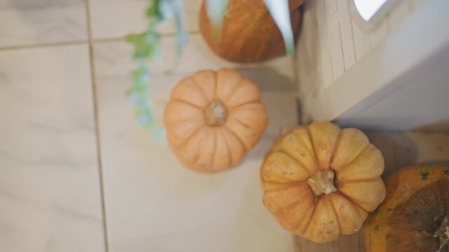 Three small pumpkins on tiled floor beside kitchen threshold and wooden step, soft natural light, trailing greenery and warm tones evoking harvest season, rustic decor and pumpkin pie baking