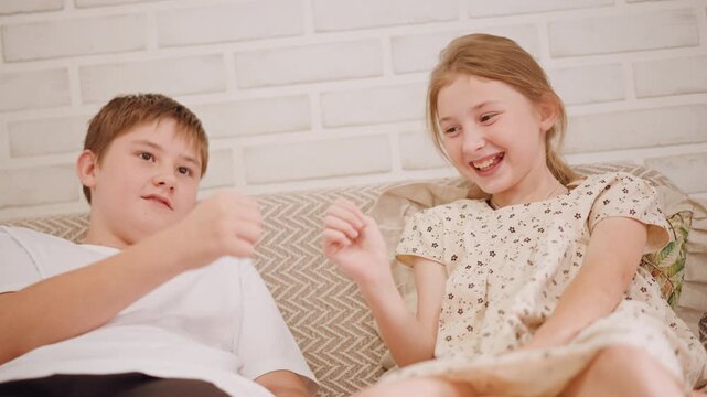 White siblings on couch taste test pumpkin pie, pointing and laughing, comparing flavors, hand gestures, casual dress, brick wall backdrop, bright sunlight, candid smiles, friendly contest mood