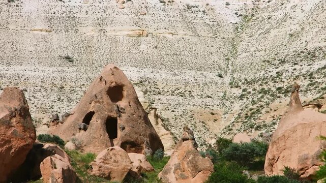 A scenic view of the unique geological rock formations, known as "fairy chimneys", in the Cappadocia region of Turkey. The landscape features rugged, arid mountainsides and ancient cave dwellings carv