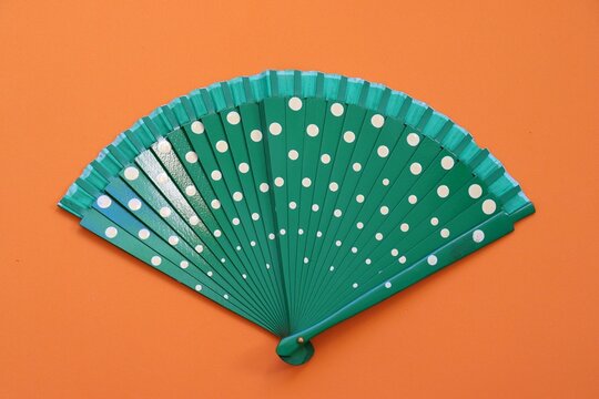 Green hand fan with white polka dots on an orange background. Vibrant color contrast and summer fashion accessory concept.