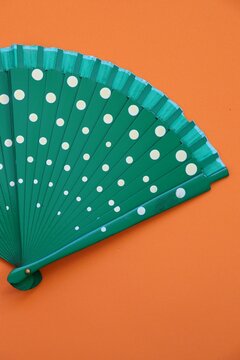 Green hand fan with white polka dots on an orange background. Vibrant color contrast and summer fashion accessory concept.