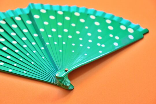 Green hand fan with white polka dots on an orange background. Vibrant color contrast and summer fashion accessory concept.
