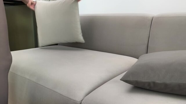 Hand uses lint roller on pillow removing hair at home. Person cleans fabric surface eliminating fur during routine indoors. Hygiene care and household cleaning concept in apartment living room..