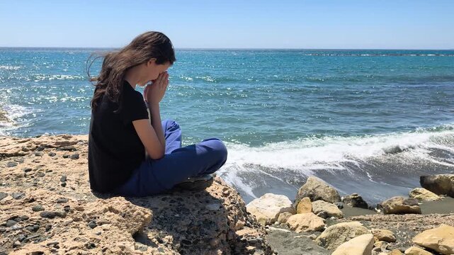 Young Christian Girl Praying with Bible by the Rocky Seashore - Slow Motion Half Speed