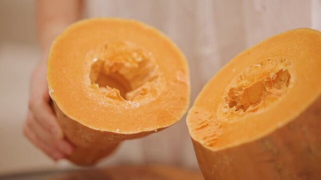 Closeup halved pumpkin flesh held by gentle hands over wooden surface, warm natural light highlights orange texture and cavity, ready for pie filling and puree, rustic autumn harvest vibe