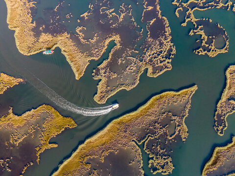 Aerial view of Dalyan River Delta with boats moving through winding channels and wetlands. Natural patterns, marsh ecosystem, tourism activity, water landscape and environmental conservation concept. 