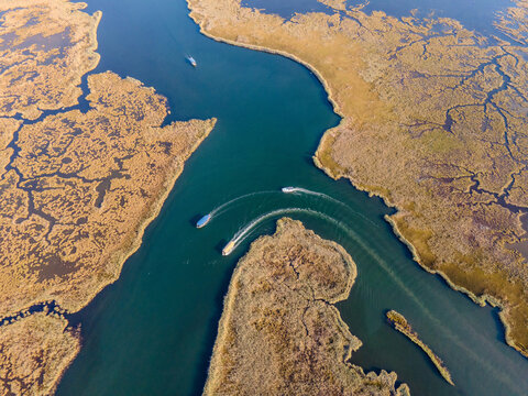 Aerial view of Dalyan River Delta with boats moving through winding channels and wetlands. Natural patterns, marsh ecosystem, tourism activity, water landscape and environmental conservation concept. 