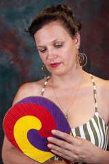 Naklejka premium Mature woman posing with a colorful circular hand fan against a dark background