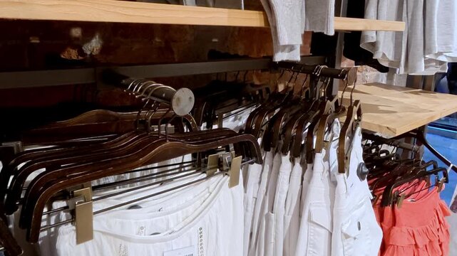  White clothing items displayed on hangers in a retail store, featuring shorts, pants, and a ruffled skirt in a vibrant color