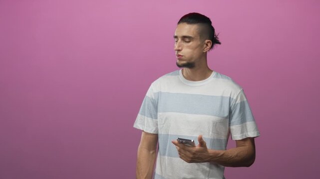 Man holding smartphone in right hand looking to the side in studio with pink backdrop; thoughtful reflection.