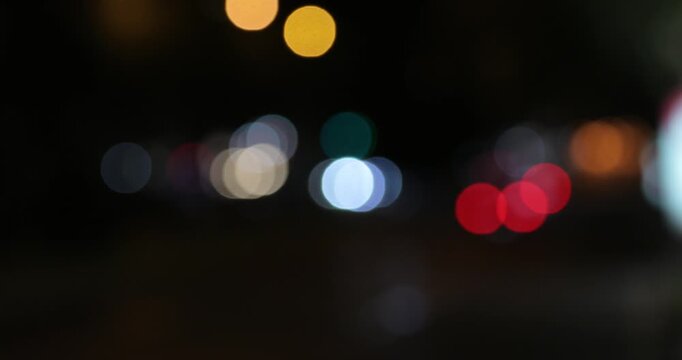Close up shot of a woman's hand in a trench coat waving to hail a cab against a beautifully blurred background of colorful city traffic lights at night.

