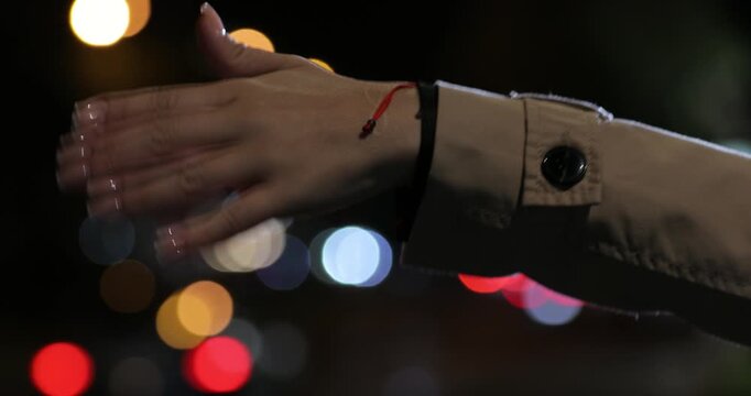 Close up shot of a woman's hand in a trench coat waving to hail a cab against a beautifully blurred background of colorful city traffic lights at night.

