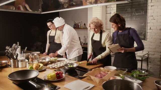 High angle shot of professional male chef helping group of women, participating in cooking master class in restaurant
