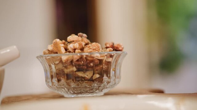 Glass bowl with pecans on wooden surface. Modern kitchen setting featuring pecan garnish in glass bowl. Stylish food presentation displaying pecan topping in glass bowl on wooden countertop