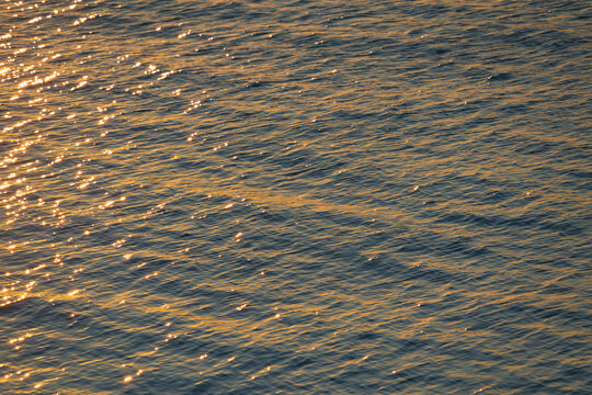 Abstract blue water surface of the Baltic Sea with golden sunset reflections creating a shimmering silk-like liquid texture