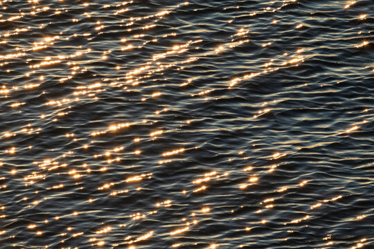 Golden sunlight sparkling on the dark blue water surface of the Baltic Sea creating beautiful glowing ripples and bokeh