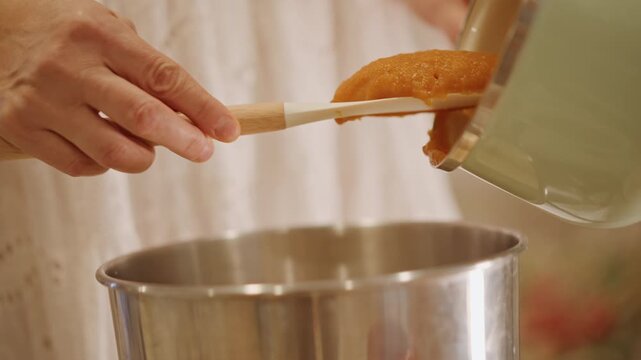 Pouring pumpkin into bowl carefully. Vintage cookware used to pour and scrape pumpkin mixture. Closeup of traditional baking scene with pouring and scraping pumpkin puree accurately