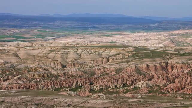 A high-angle shot captures the expansive and otherworldly landscape of Cappadocia, a historical region in Turkey known for its distinctive geological formations, deep ravines, and valleys. The terrain
