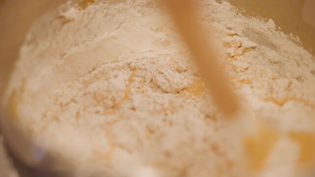 Cooking batter with energetic movements. Close perspective of blending flour into pumpkin filling with tools. Upclose view of vigorous folding of flour into pumpkin mixture using silicone spatula