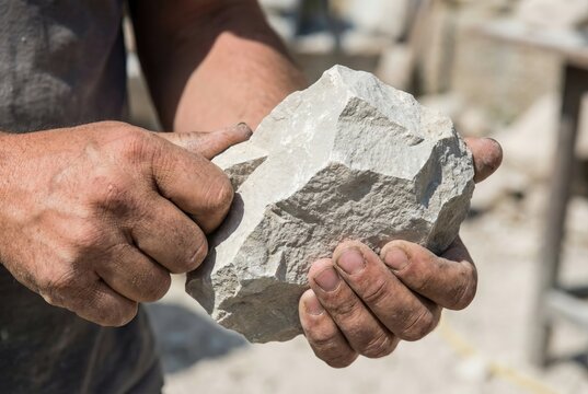 Dirty hands holding a large rough chunk of raw light colored limestone rock