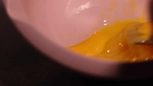 Horizontal video close up. Chef beats and stirs egg yolks with fork in pink bowl on kitchen table. Concept of cooking lunch, dinner, crepes, omelet, scrambled eggs for Slavic Maslenitsa, Mardi Gras