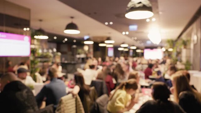 Large event with mingling attendees. Busy indoor dining scene featuring socializing and table arrangements. Vibrant indoor event with numerous participants engaging at tables under warm lighting