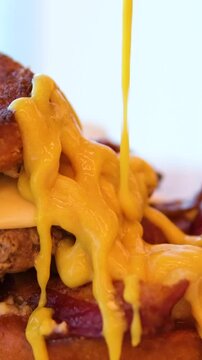 to pour mustard on layers of a Reuben sandwich filled with corned beef, Swiss cheese, and sauerkraut, placed on a wooden board, highlighting a tasty meal perfect for lunchtime.