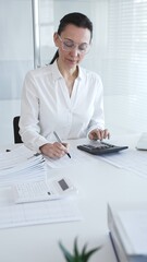 A close-up of a calculator on an office desk. A professional woman enters and analyzes financial...