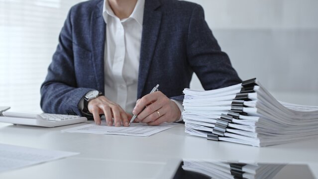 Accountant or bookkeeper calculating financial data, preparing taxes, managing business reports, and organizing paperwork with a calculator and stack of documents on an office desk. Audit and taxes
