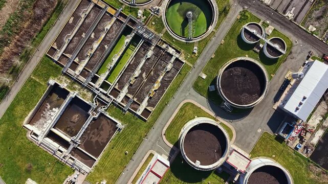 The view shows a water treatment facility with different types of tanks and equipment. The site is organized with green spaces around the structures and roads for vehicles.