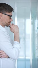 Fototapeta premium Male professional wearing eyeglasses planning business strategy, brainstorming ideas, and creating a mind map on a clear glass whiteboard in a modern office