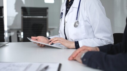 Fototapeta premium Female doctor consulting patient man using digital tablet, discussing medical records in modern clinic office, healthcare technology. Medicine, healthcare and science concept