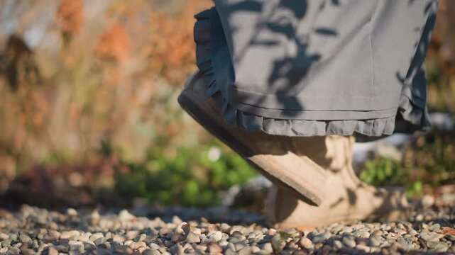 Homeward walking feet on gravel path closeup of skirt hem and wool boots crunching leaves soft sunlight casting shadow patterns slow measured steps returning toward kitchen prep rustic backyard