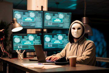 Hacker wearing mask and hood to hack computer system, breaking into company servers to steal big data. Masked man looking dangerous and scary, impostor creating security malware. © DC Studio