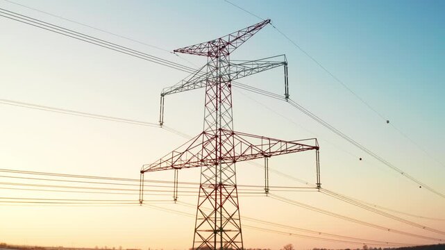 Aerial view of electricity transmission towers in a snowy field during sunset, symbolizing energy infrastructure and green energy distribution.