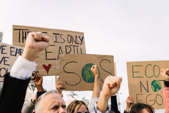 Activists raising fists and holding cardboard signs at a protest, advocating for environmental protection and action against climate change, expressing urgency for global responsibility