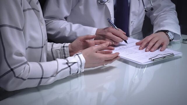 Doctor talking with a patient during a medical consultation, discussing health issues and treatment options while reviewing forms at a clinic desk. Overwork in medicine