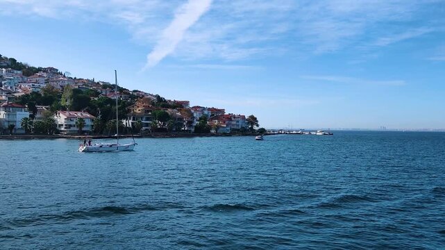 Scenic View of a White Sailing Boat Near the Shore of Kinaliada Island with Seagulls Flying Over the Blue Marmara Sea and Waterfront Houses in the Background, Istanbul