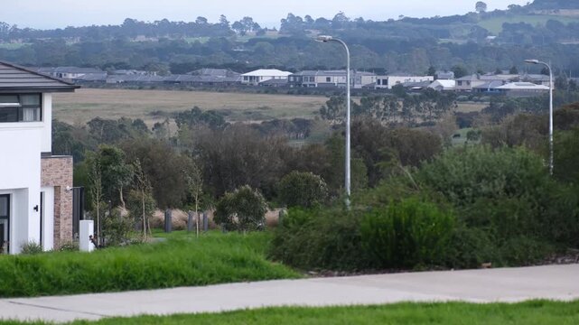 Greenvale, an outer northern Melbourne suburb on a windy day. Built contemporary homes alongside undeveloped dry grassland paddocks and native scrubland under a grey overcast sky